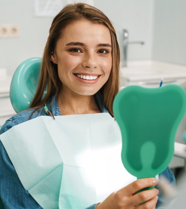 European young woman smiling while looking at mirror in dental clinic man smiling in dentists chair