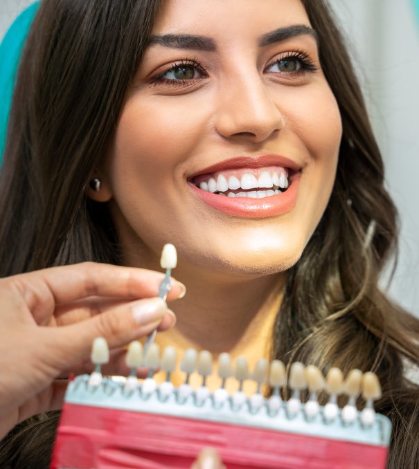 Young woman with perfect teeth , looking how white are her teeth , with teeth shade man smiling in dentists chair